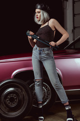 full length view of stylish blonde woman in beret looking away while changing car wheel