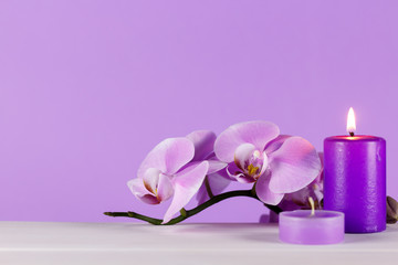 Pale purple orchid on a white table with purple background. Scented candles on the table one of the two ignited