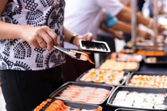 Hand picking sushi roll from food stall at event street market
