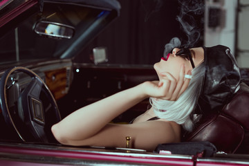 side view of sensual blonde woman in sunglasses and beret smoking cigarette in retro car