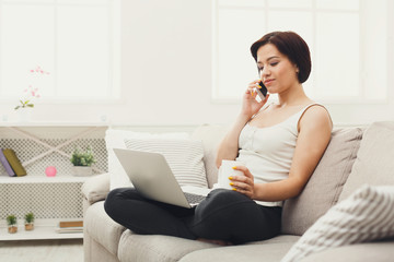 Girl with laptop and mobile sitting on beige couch.