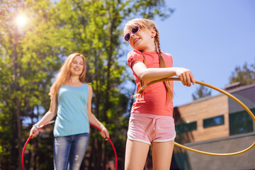 Healthy routine. Adorable little girl hula-hooping together with her mother and grinning happily...