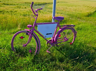 Naklejka premium Rosa angemaltes Fahrrad mit einer weißen, bis auf einen schwarzen Pfeil, unbeschrifteten Werbefläche.