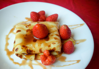 Sweet pancake on a plate decorated with strawberries and poured with caramel syrup. 