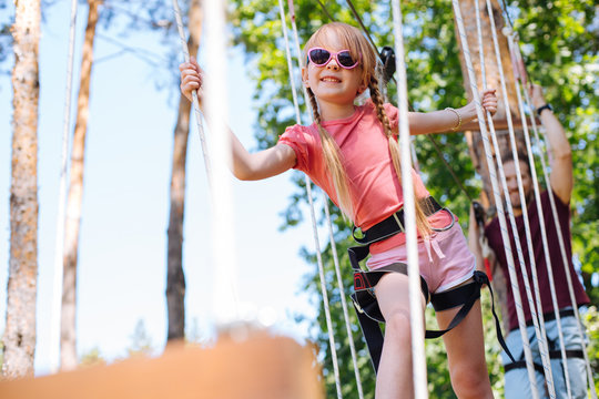 Brave Kid. Adorable Little Girl Confidently Walking Down The Rope Park Trail And Having Fun While Her Father Following Her