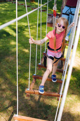 Full of confidence. Charming little girl posing for the camera while going down rope park trail during a family day at an adventure park
