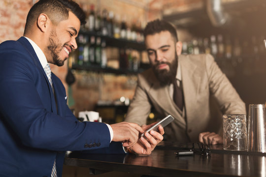 Businessman Showing Information On Phone To Barman