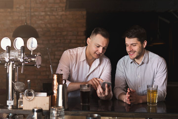 Friends enjoying fresh beer at pub and sharing mobile
