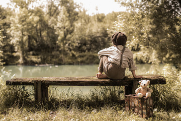 Junge sitzt auf einer Bank am Weiher