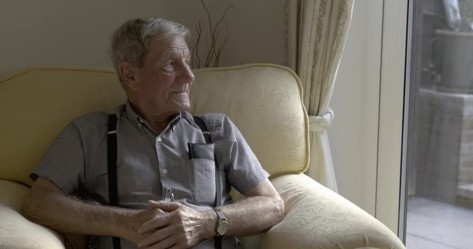 Seniors portrait, contemplative old caucasian man staring outside. Sat in an arm chair next to a window.