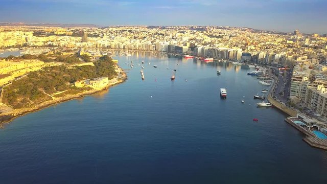 Valletta, Malta - 4K flying above Marsamxett Harbour with lots of traditional maltese boats. Manoel Island, Sliema and Gzira at background with early in the morning warm sunlight