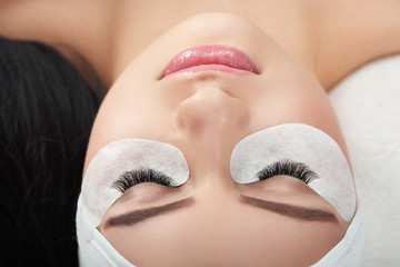 Photo comparison of woman's normal and fake enlarged lashes. Client lying on special coach wearing...