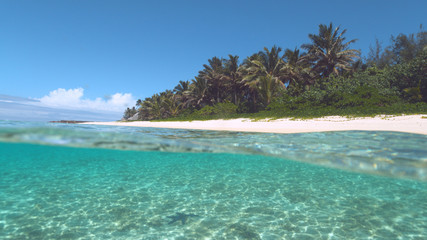 Fototapeta na wymiar HALF UNDERWATER: Tranquil turquoise ocean washes the idyllic white sand beach.