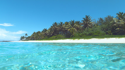 Glassy ocean water glistens in the bright summer sunshine near tropical island