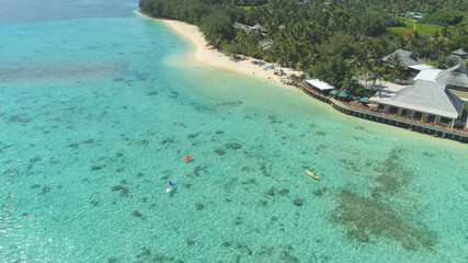 Fototapeta na wymiar AERIAL: Tourists paddleboard and canoe in the turquoise ocean near luxury hotel.