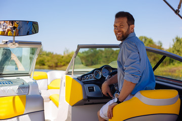 Proud owner. Pleasant young man posing behind a steering wheel of a yacht and smiling, being proud...