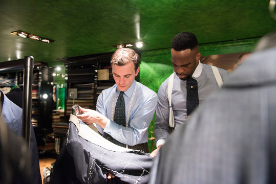 Tailor and customer looking at unfinished bespoke jacket in traditional tailors shop