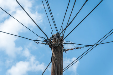 Power line old retro style wooden pole with many electric supply wires or cables against blue sky....