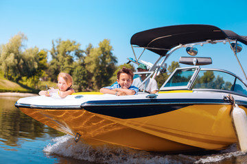 Naklejka premium Breathtaking view. Joyful little siblings sitting on the bow of the boat and contemplating the view while smiling happily