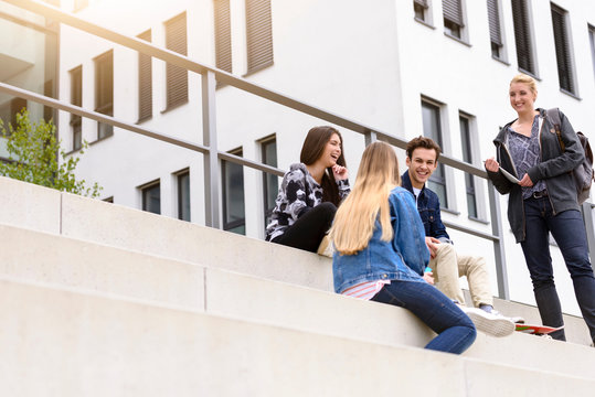 Four young adult students sitting chatting on stairway outside college, low angle view