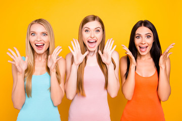 Portrait of mad funny girls yelling with wide open mouth full of happiness gesturing with palms enjoying seasonal discounts isolated on bright yellow background