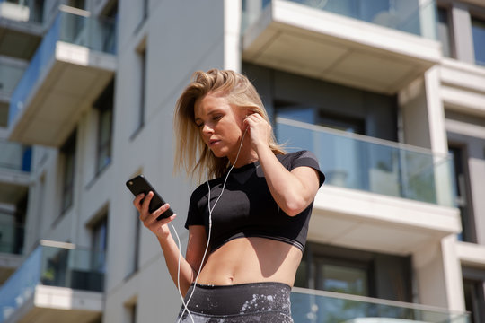 Young woman listening to music on mobile phone, building in background