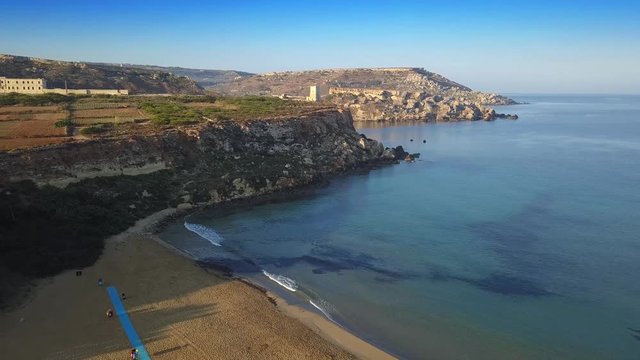 Ghajn Tuffieha, Malta - The beautiful beach of Golden Bay at sunrise, flying towards Ghajn Tuffieha Watch Tower