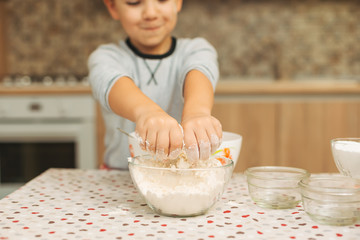Boy hands in a glass bowl with flour on the kitchen table with h