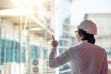 Young Asian Engineer or Architect pointing while wearing protective equipment safety helmet at construction site. Engineering, Architecture and construction business concepts