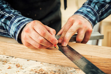 Close-up The man measures a wooden board with a ruler and marks with pencil the necessary points for slices