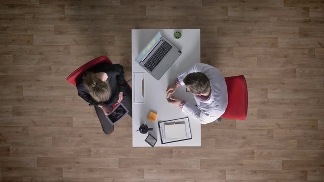Doctor giving ultrasound to pregnant young mother, topshot, sitting at table with laptop in office