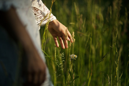 Image of female hand in tall grass on forest glade. Hand of girl dressed in pretty white short lace dress touches grass in nature park.