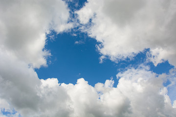 Piece of blue sky surrounded by white fluffy clouds, background