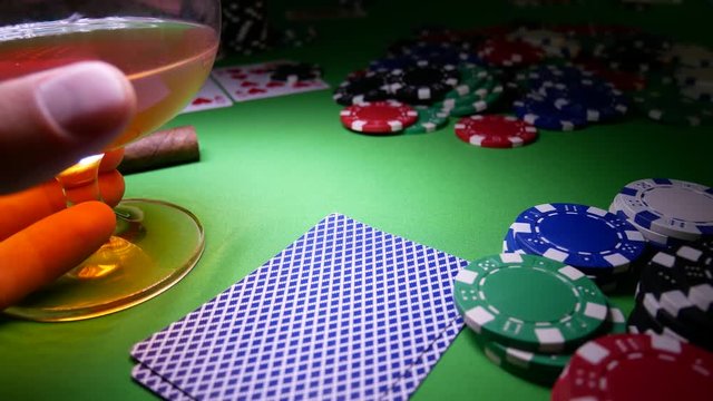 Poker Player is Nervous and Makes Bet in Poker. Cigar and Glass with Brandy On The Poker Table With Poker Chips. Cards On Table In Casino
