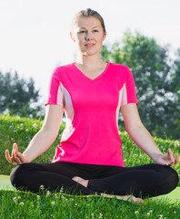 Adult female in pink T-shirt is sitting and doing meditation