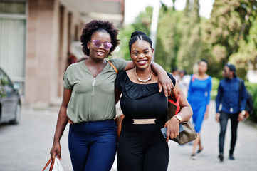 Two african american girls walking and posed at street of city.
