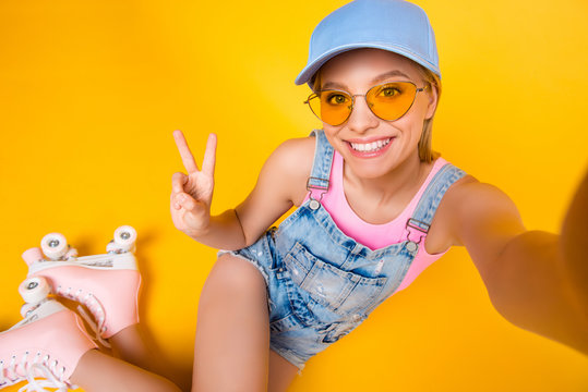 Self portrait of positive toothy girl shooting selfie on front camera wearing roller skates gesturing v-sign with hand isolated on yellow background, fitness workout athletic sport concept