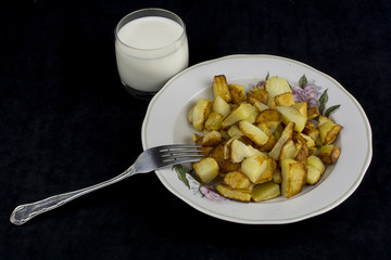 fried potatoes with a glass of milk on a dark background