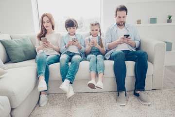 Portrait of family with two kids having holding smart phone electronic device in hands texting sms...