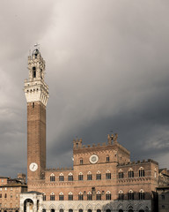 Palazzo Pubblico and Mangia tower against overcast sky in the historic center of Siena, Italy