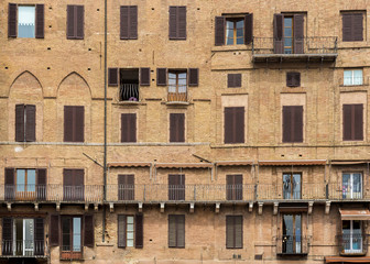 Exterior of a medieval building with windows and balconies in Siena, Italy