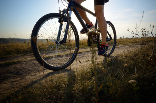 Male cyclist driving by rural dirt road outdoors. Low angle view