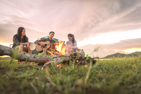 Group of travelers camping and doing picnic and playing music together. Mountain and lake background. People and lifestyle. Outdoors activity and leisure theme. Backpacker and Hiker. Dawn and twilight