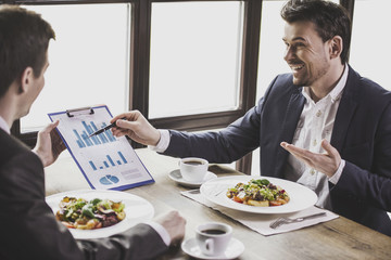Two businessmen have lunch with coffee in cafe.