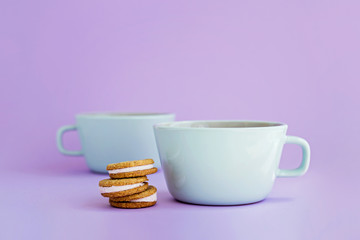 Two big cups of coffee and sandwich cookies on violet background.