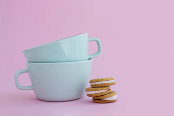 Two big cups of coffee and sandwich cookies on pink background.