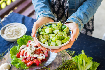 Woman hands holds fresh summer cucumber salad with black pepper and rock salt covered with olive unrefined oil. Raw vegan vegetarian healthy food 