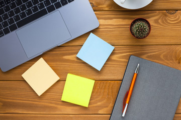 Laptop, white cup of coffee, cactus, snacks and notebook on the bright wooden background. Business, office, education, planning concept. Top view. Close up.