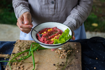 Woman hands holds spicy red beetroot Israeli chickpea hummus with herbs and covered with olive oil. Traditional mediterranean food used with vegetables. Vegan vegetarian healthy food.