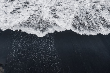 white ocean foam on black sand volcanic texture